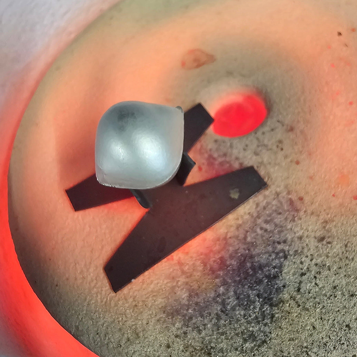 Glass piece on a small steel stand, being worked on a soldering block in the studio