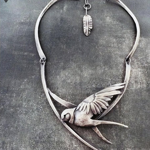 Silver bird-shaped necklace on a textured gray background