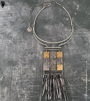 Necklace with geometric pendant and fringes on a textured gray background