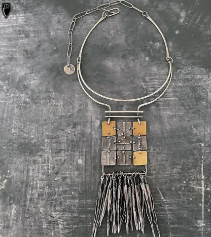 Necklace with geometric pendant and fringes on a textured gray background
